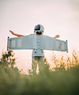 Boy wearing toy airplane wings playing game pretending to fly imagining travel freedom having fun outdoors in sunny park