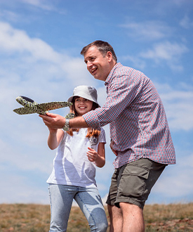 Cheerful young girl and her dad having fun with model airplane